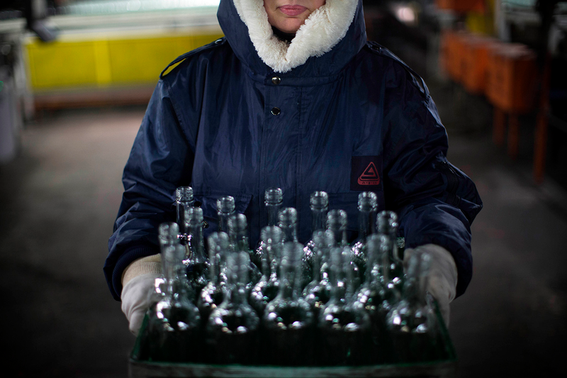 An employee carries a box of defective glass bottles to be recycled.